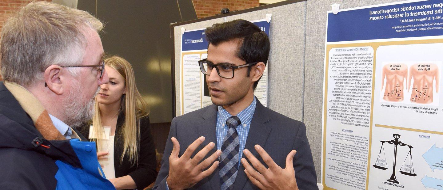 Student wearing a blue suit presenting his project to a professor